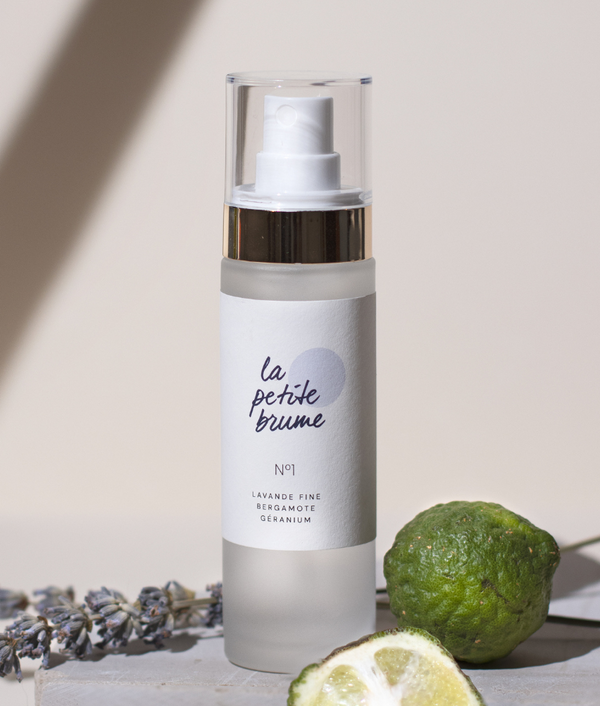 Brume d'oreiller en spray avec etiquette blanche sur fond beige avec de la lavande et des citrons verts a cote